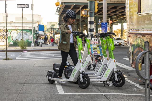 A woman parks an electric scooter on a sidewalk in an area outlined with white paint
