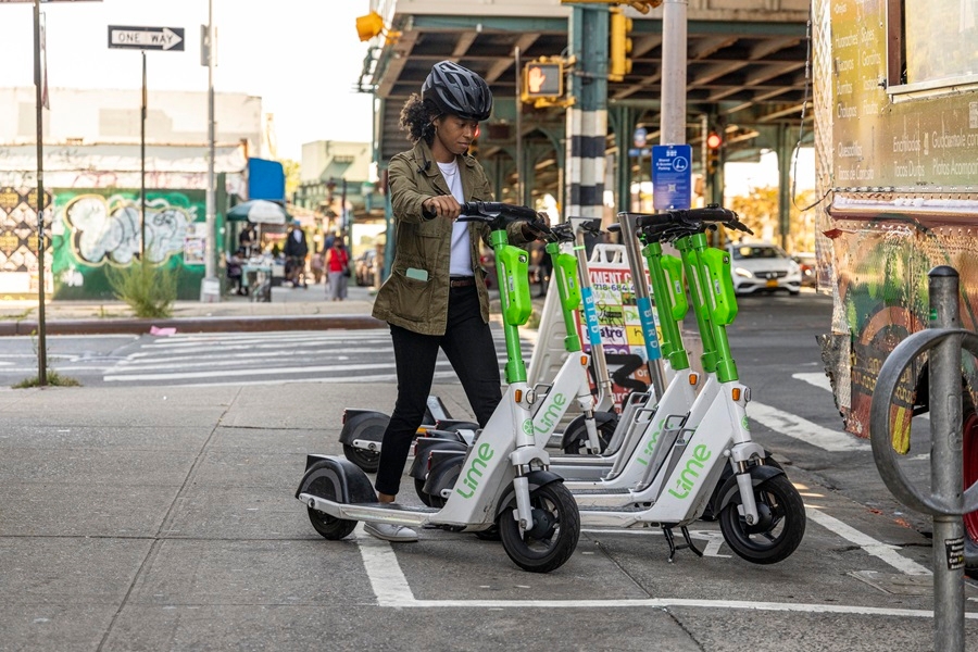 A woman parks an electric scooter on a sidewalk in an area outlined with white paint